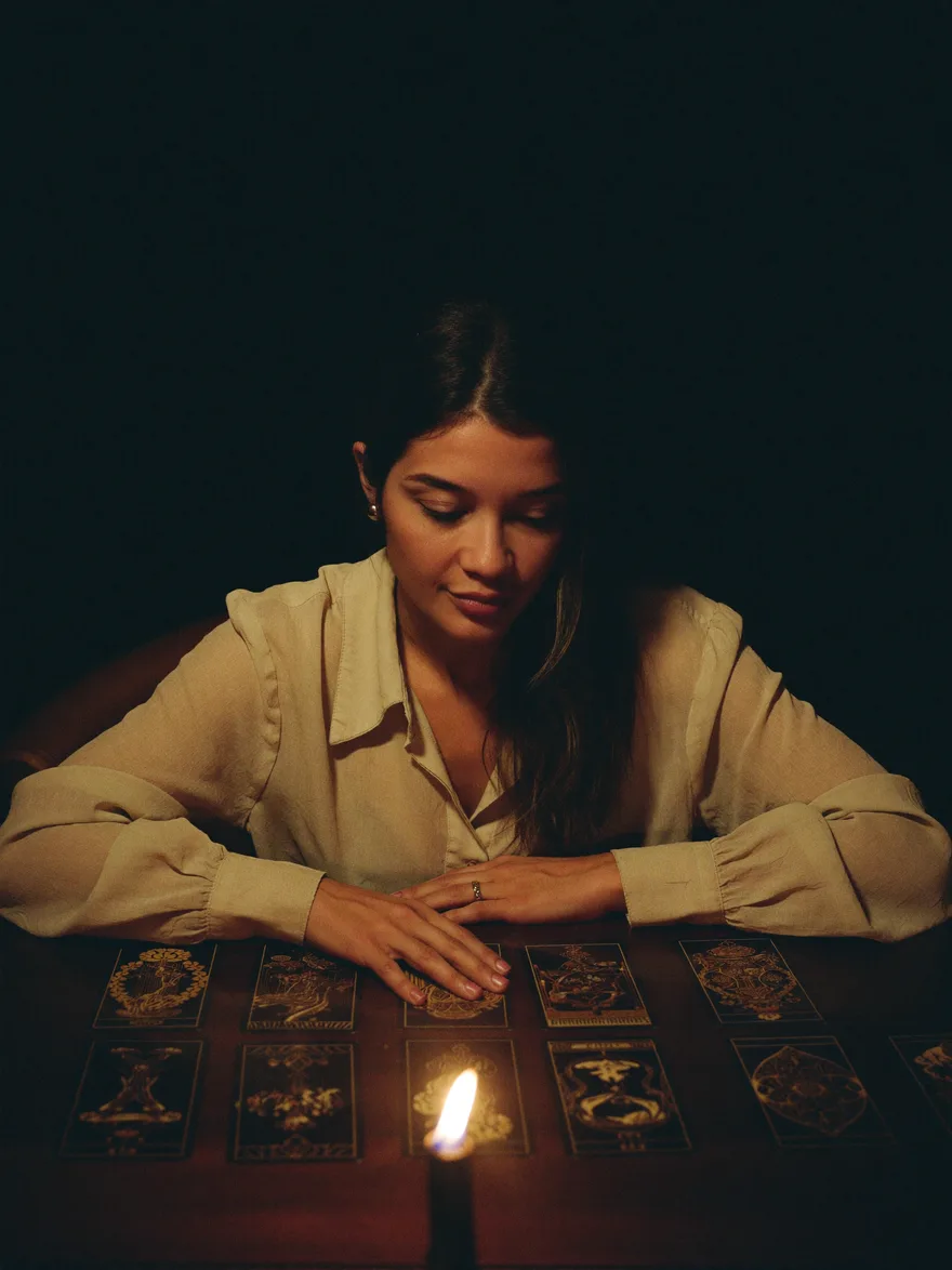 Vitoria Purcini à mesa, à luz de vela, abrindo uma tiragem de cartas de tarô